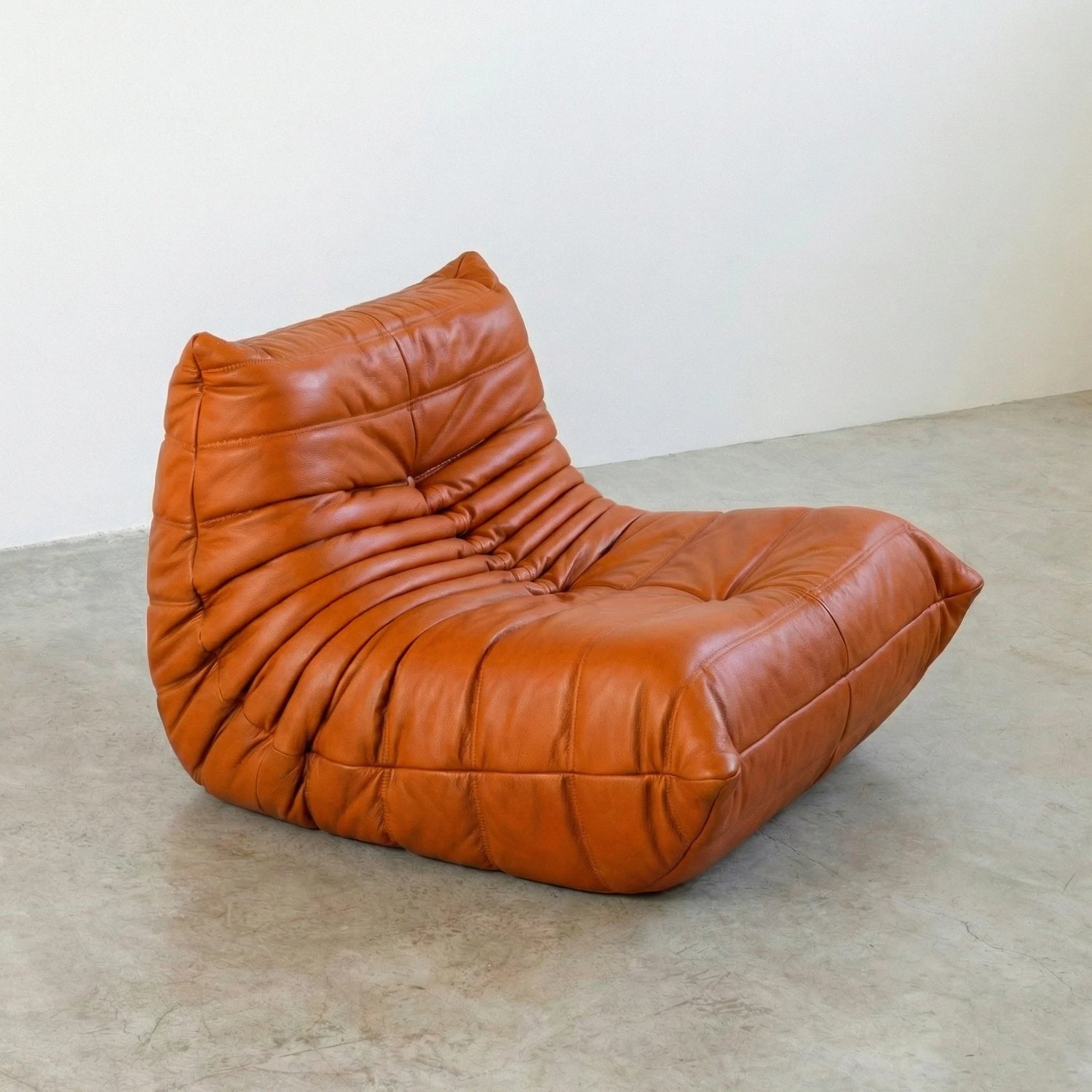 Togo Chair Dupe in cognac real cowhide leather on a concrete floor with a white wall background