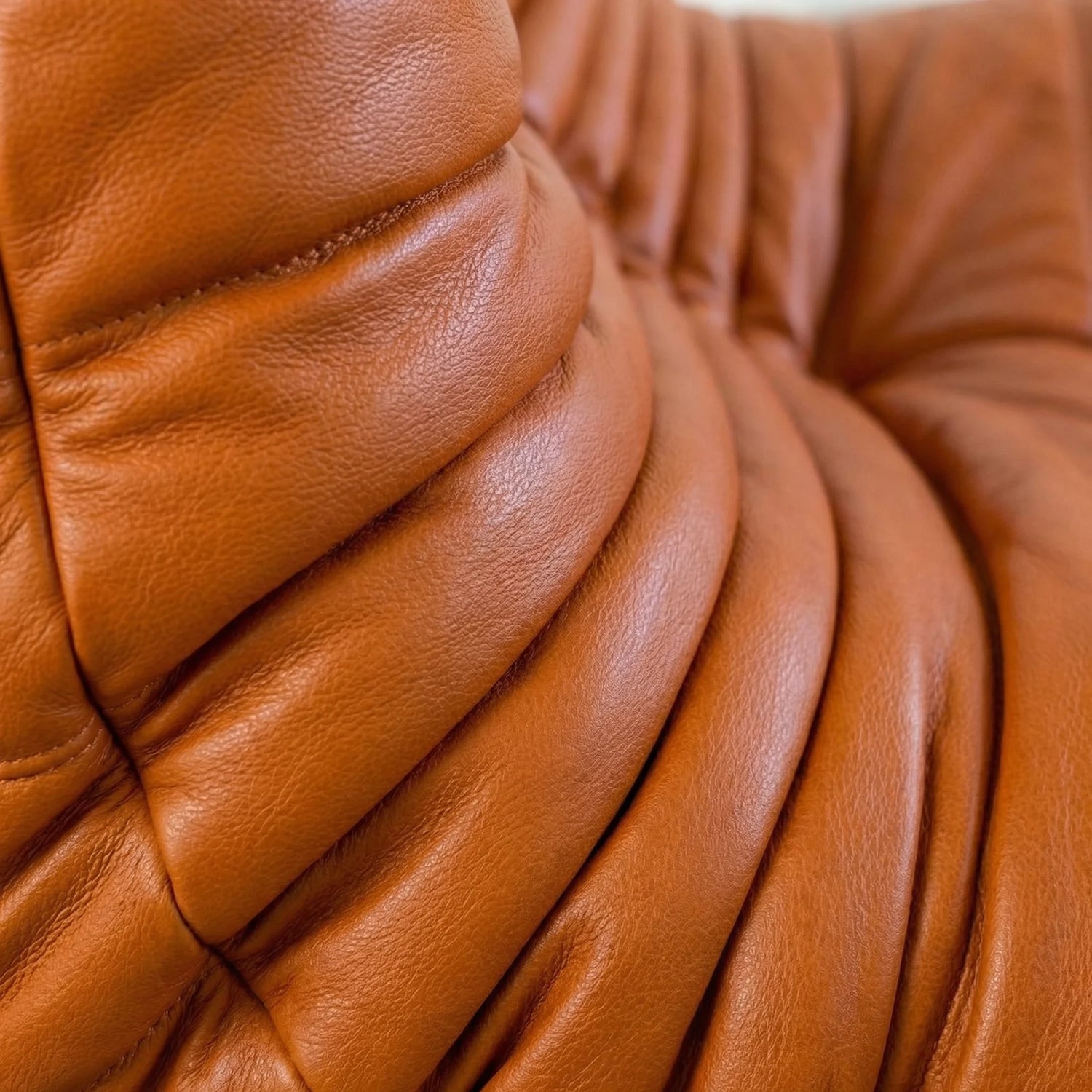 Close-up of the Togo Chair Dupe in cognac real cowhide leather on a concrete floor with a white wall background