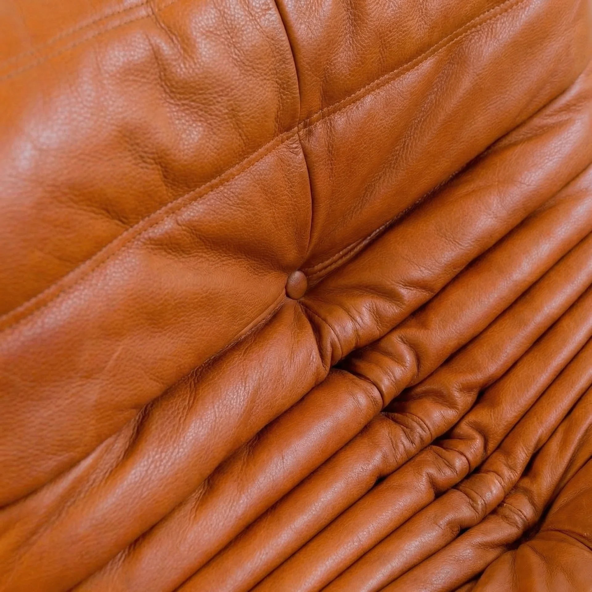 Close-up of the Togo Chair Dupe in cognac real cowhide leather on a concrete floor with a white wall background