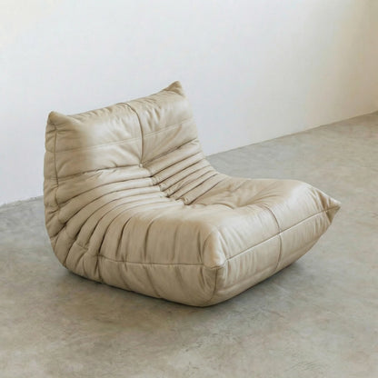 Togo Chair Dupe in cream real cowhide leather on a concrete floor with a white wall background