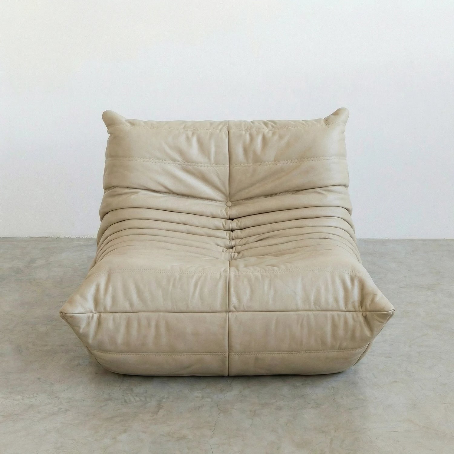 Togo Chair Dupe in cream real cowhide leather on a concrete floor with a white wall background