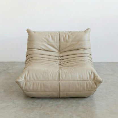 Togo Chair Dupe in cream real cowhide leather on a concrete floor with a white wall background