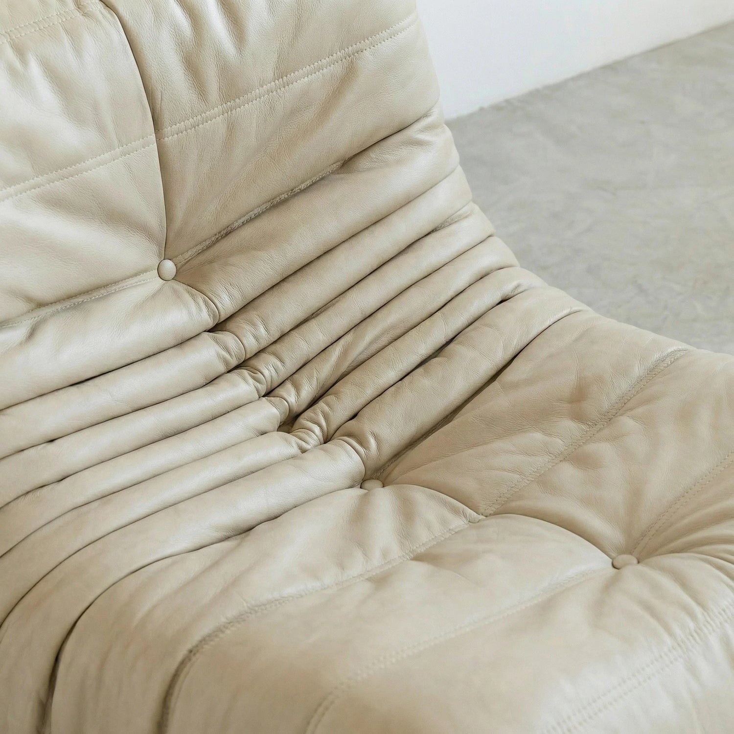 close-up of the Togo Chair Dupe in cream real cowhide leather on a concrete floor with a white wall background