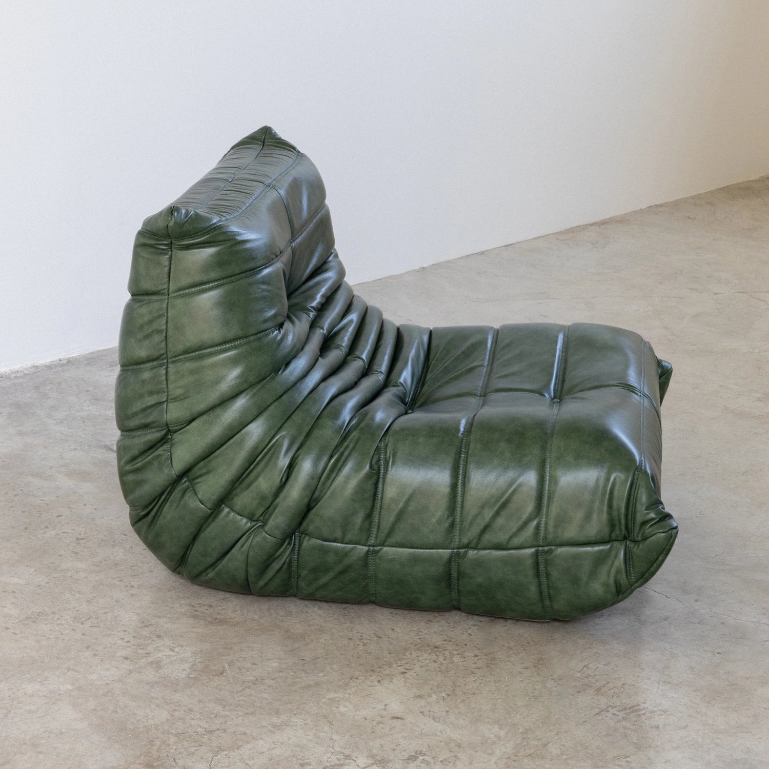 Togo Chair Dupe in green real shiny oil wax leather on a concrete floor with a white wall background