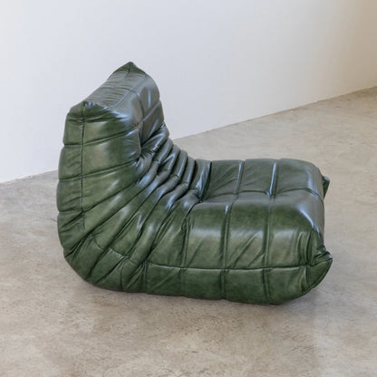 Togo Chair Dupe in green real shiny oil wax leather on a concrete floor with a white wall background