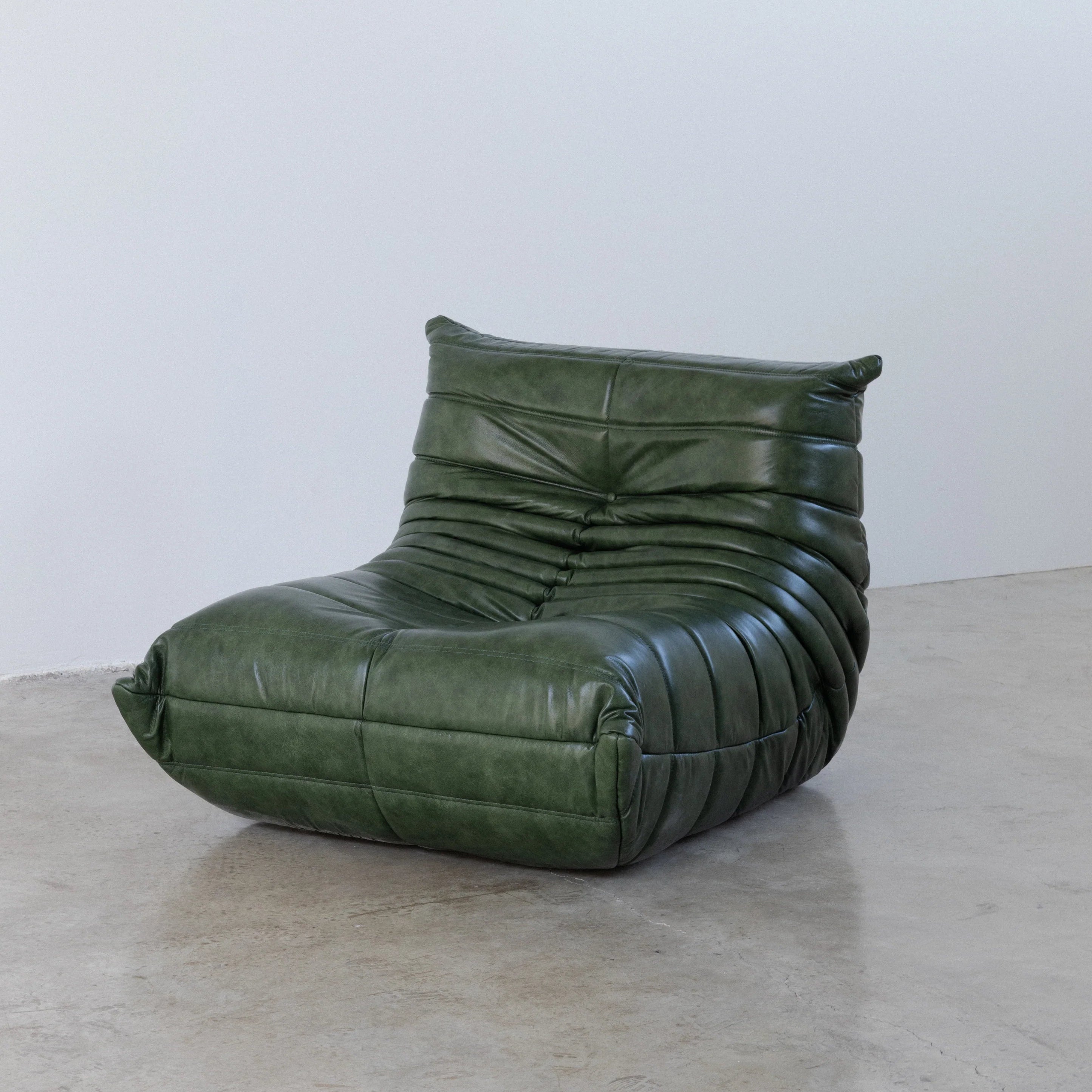 Togo Chair Dupe in green real shiny oil wax leather on a concrete floor with a white wall background