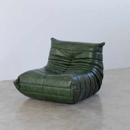 Togo Chair Dupe in green real shiny oil wax leather on a concrete floor with a white wall background