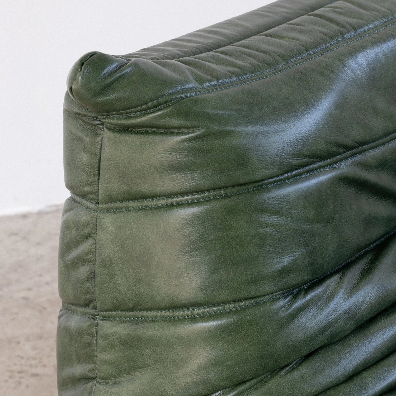 Close-up of the green leather togo couch dupe with visible stitching on a neutral background