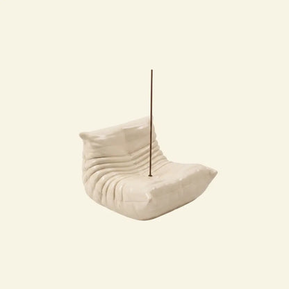 Cream Bruma incense holder shaped like a pleated lounge chair with an incense stick on a soft beige background.