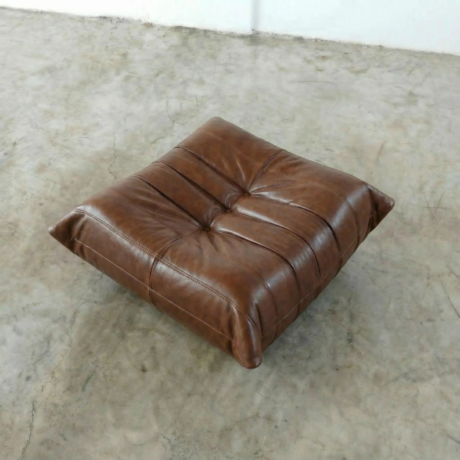 Brown togo leather ottoman dupe on a textured floor