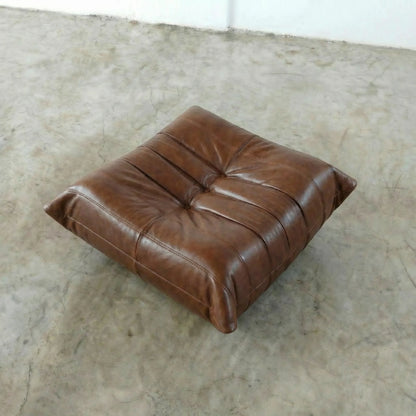 Brown togo leather ottoman dupe on a textured floor
