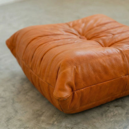 Cognac real leather togo ottoman dupe  on a concrete floor