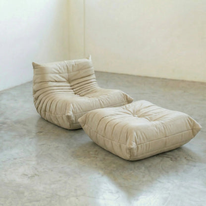 Beige togo leather chair dupe and ottoman on a concrete floor with white walls.