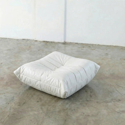 White togo ottoman dupe on a concrete floor with a white wall background