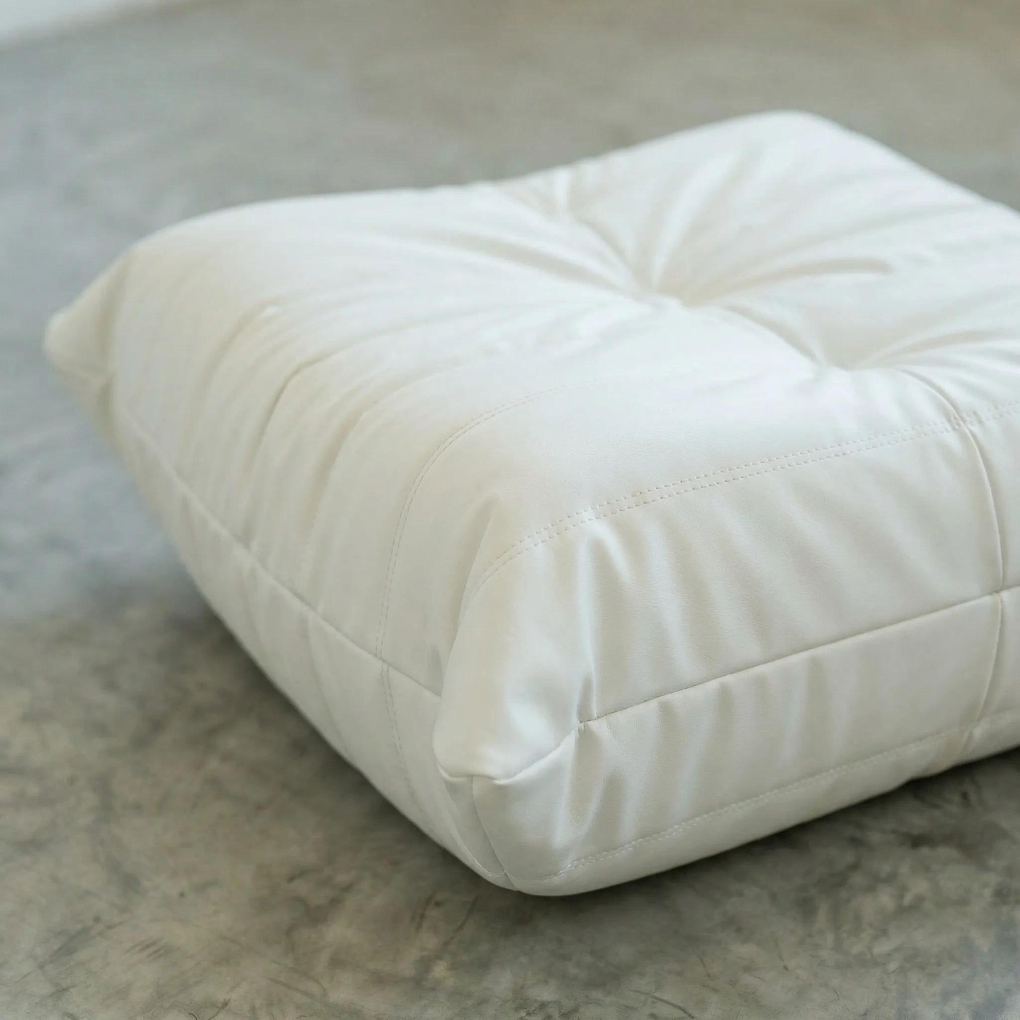 White togo ottoman leather dupe on a concrete floor with a white wall background