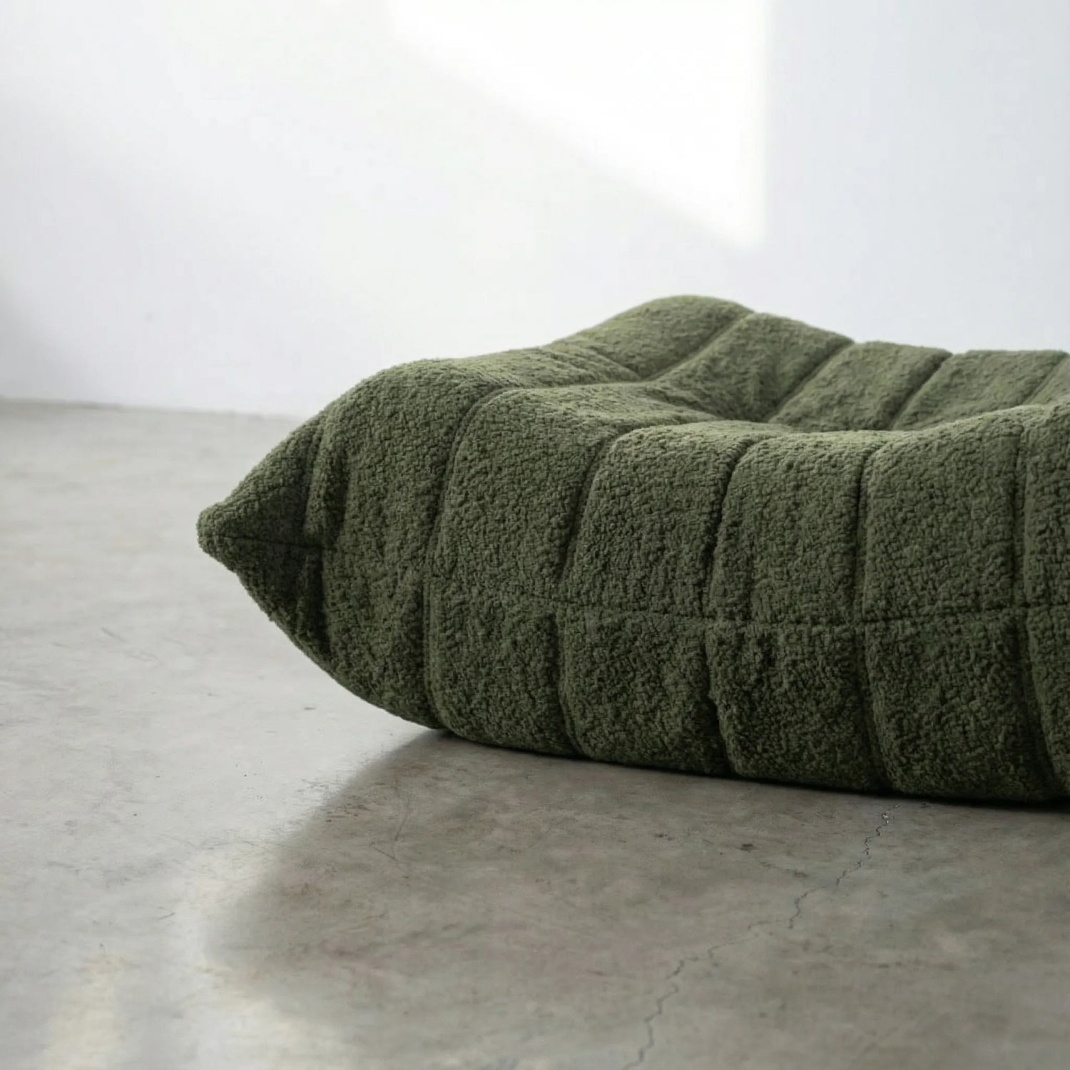 Close-up of dark green togo ottoman replica in bouclé on a concrete floor.