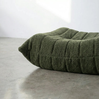 Close-up of dark green togo ottoman replica in bouclé on a concrete floor.