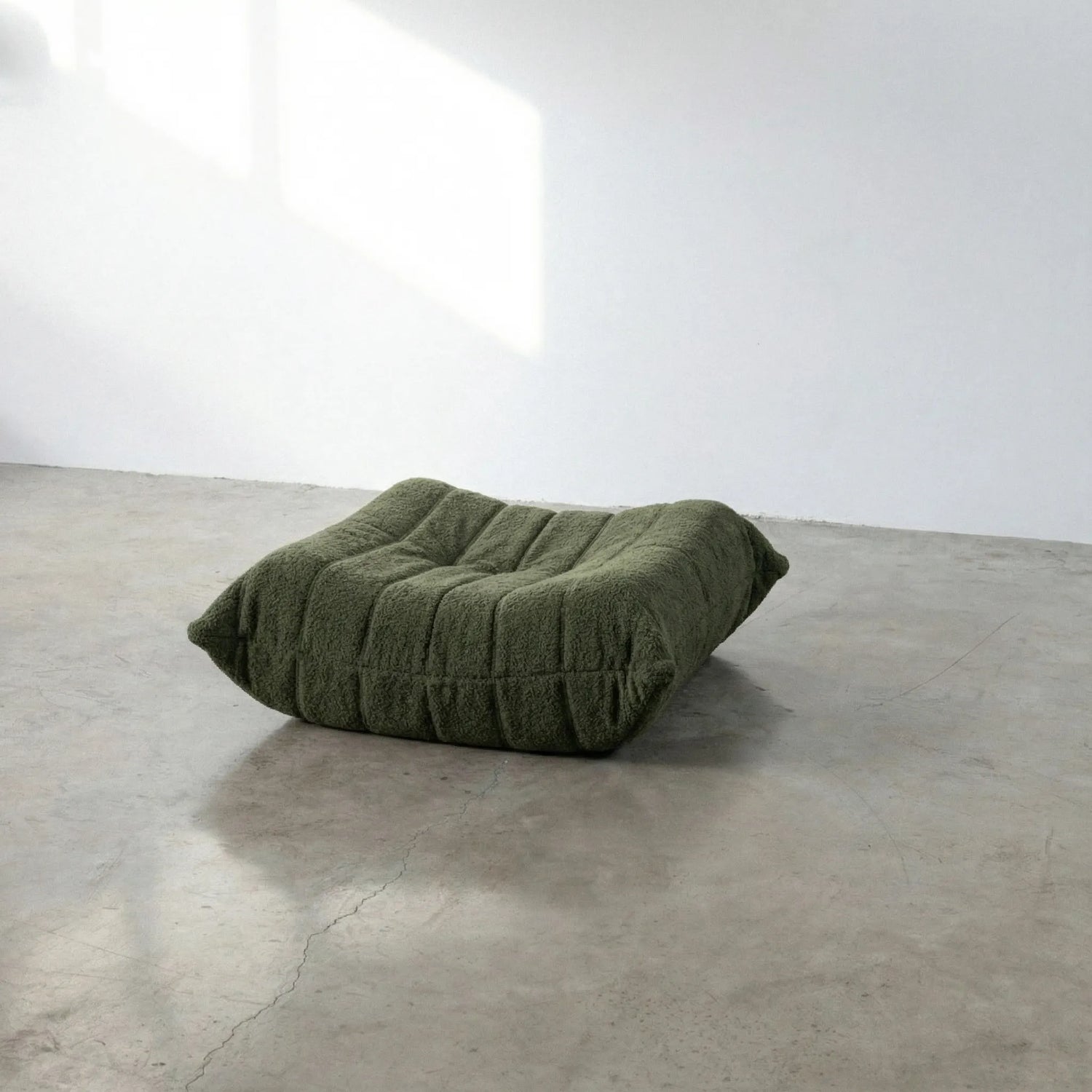 Green togo-styled ottoman dupe in bouclé by vibehaus on a concrete floor with white walls