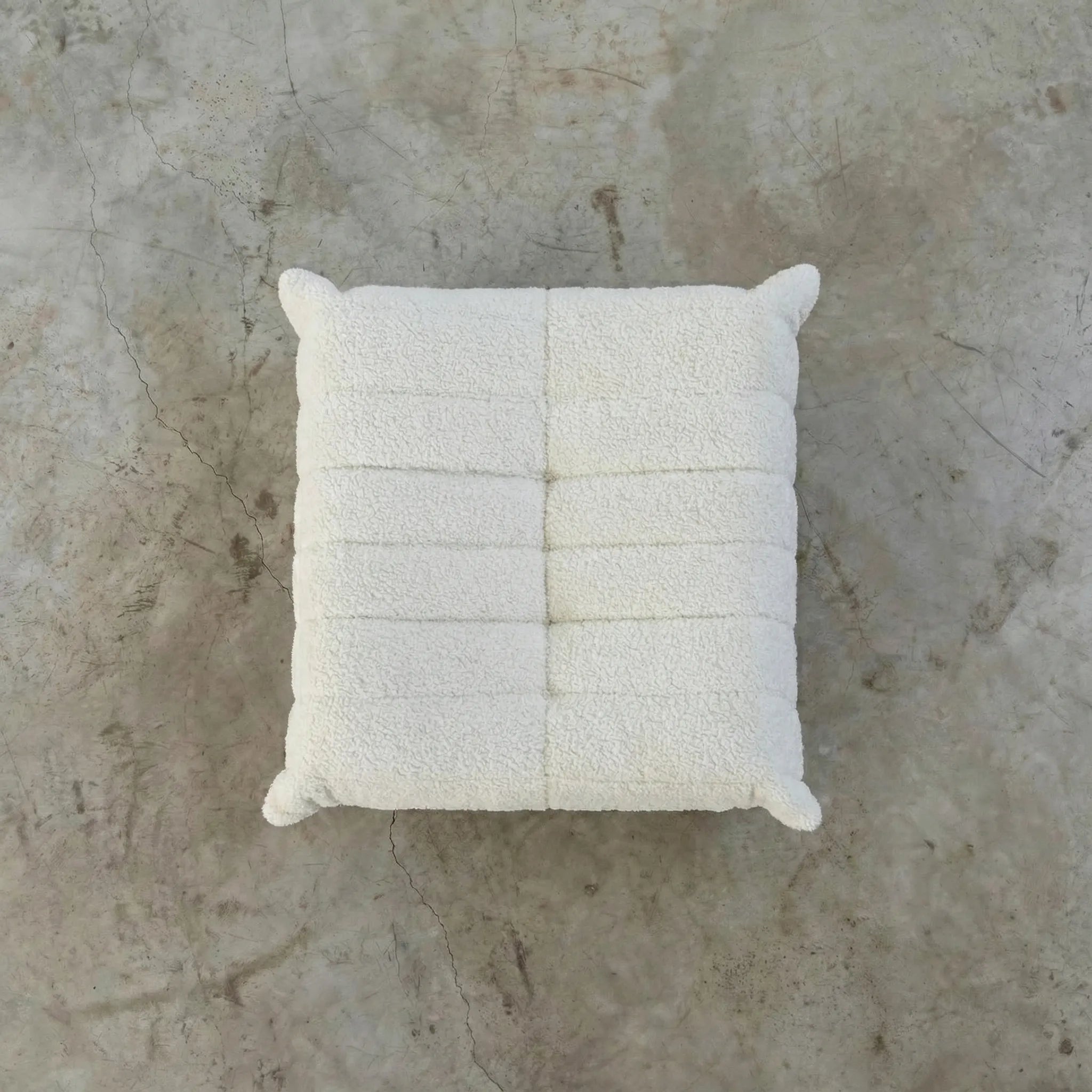 Top angle image of a white togo ottoman replica in bouclé on a concrete floor.