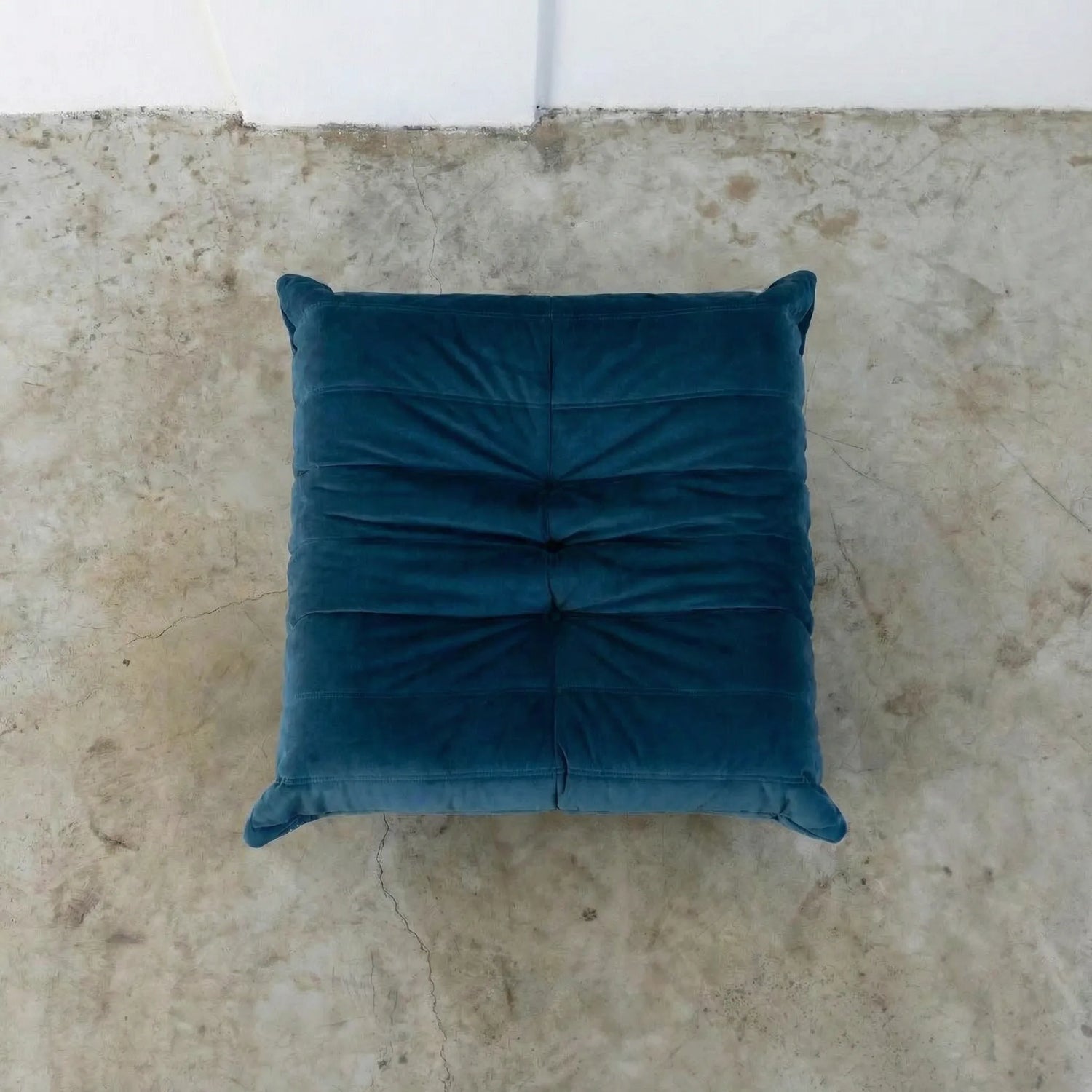 Dark blue togo ottoman replica in velvet suede on a concrete floor.