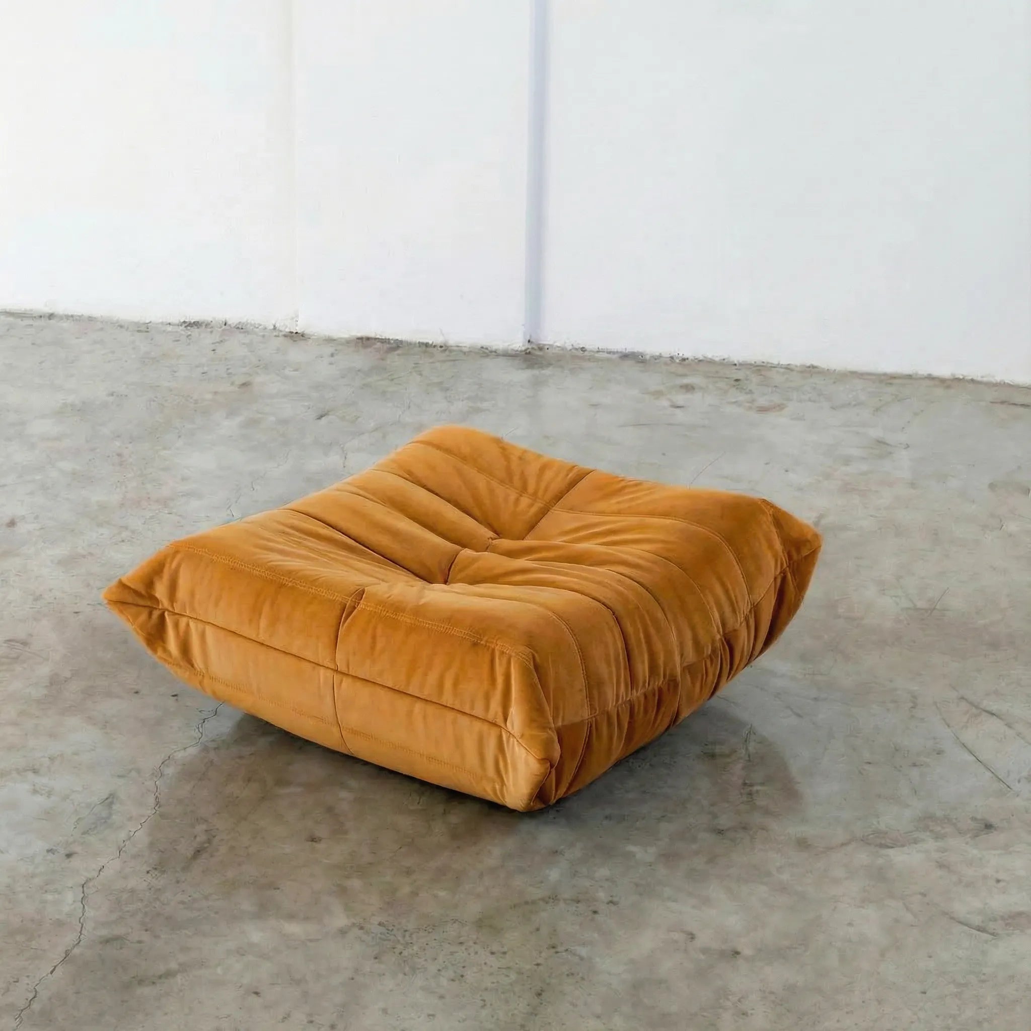 Orange togo-styled ottoman dupe in velvet suede by vibehaus on a concrete floor with white walls