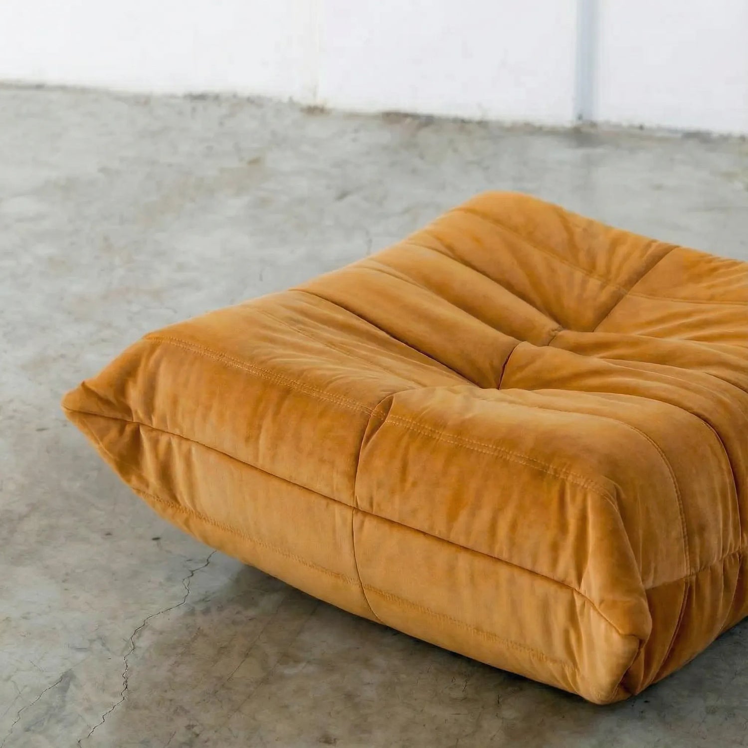 Close-up of orange togo ottoman replica in velvet suede on a concrete floor.