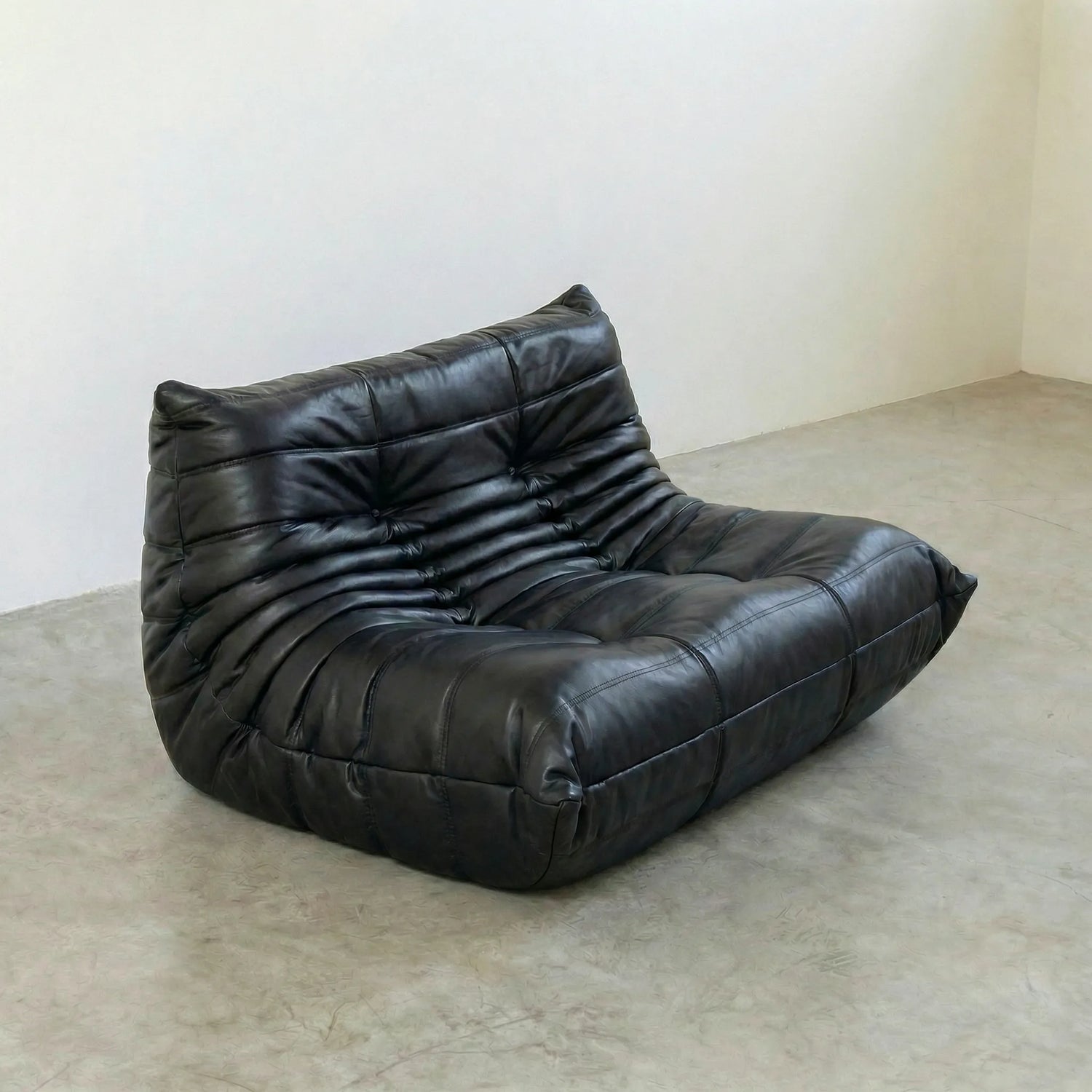togo sofa dupe in black leather on a concrete floor with a white wall background