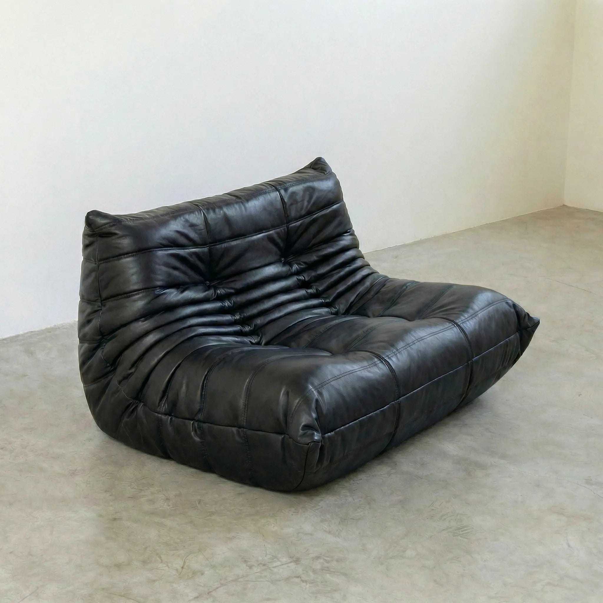 togo sofa dupe in black leather on a concrete floor with a white wall background