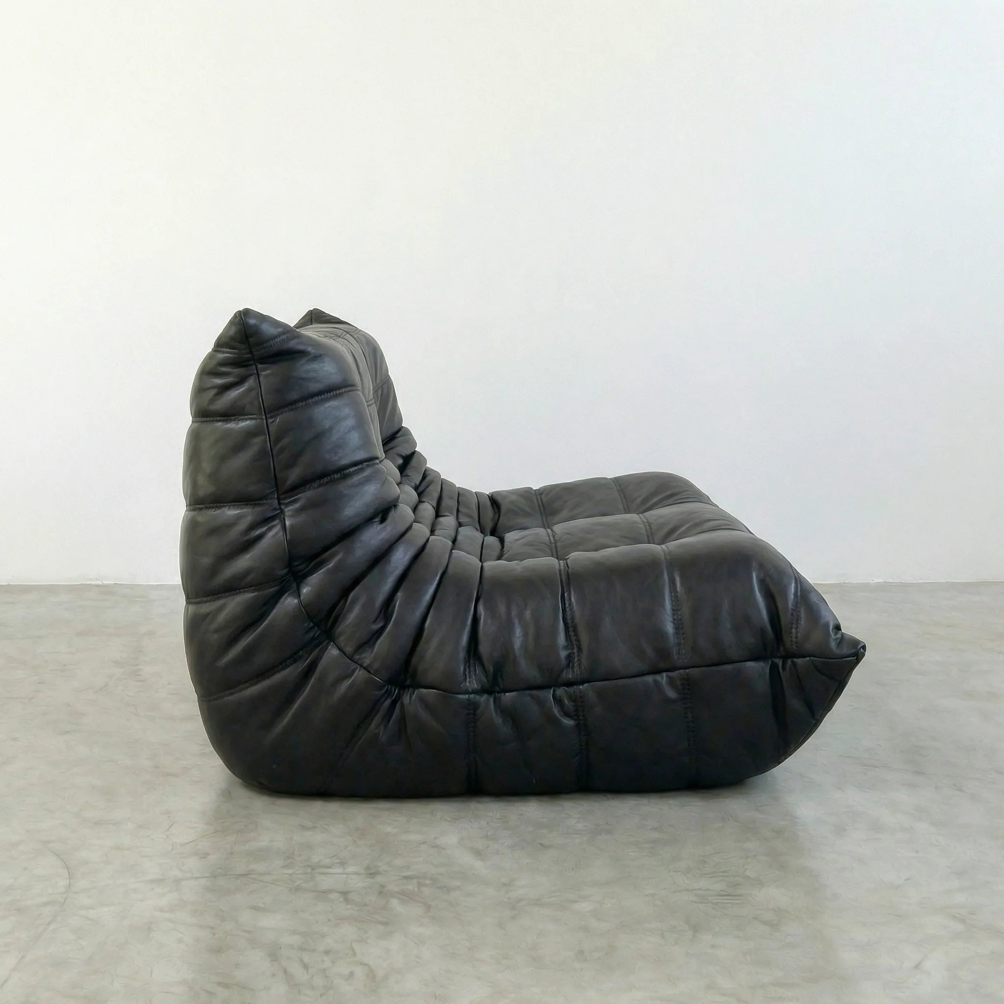 togo sofa dupe in black leather on a concrete floor with a white wall background