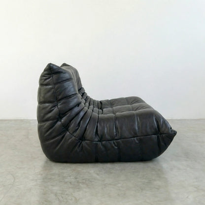 togo sofa dupe in black leather on a concrete floor with a white wall background