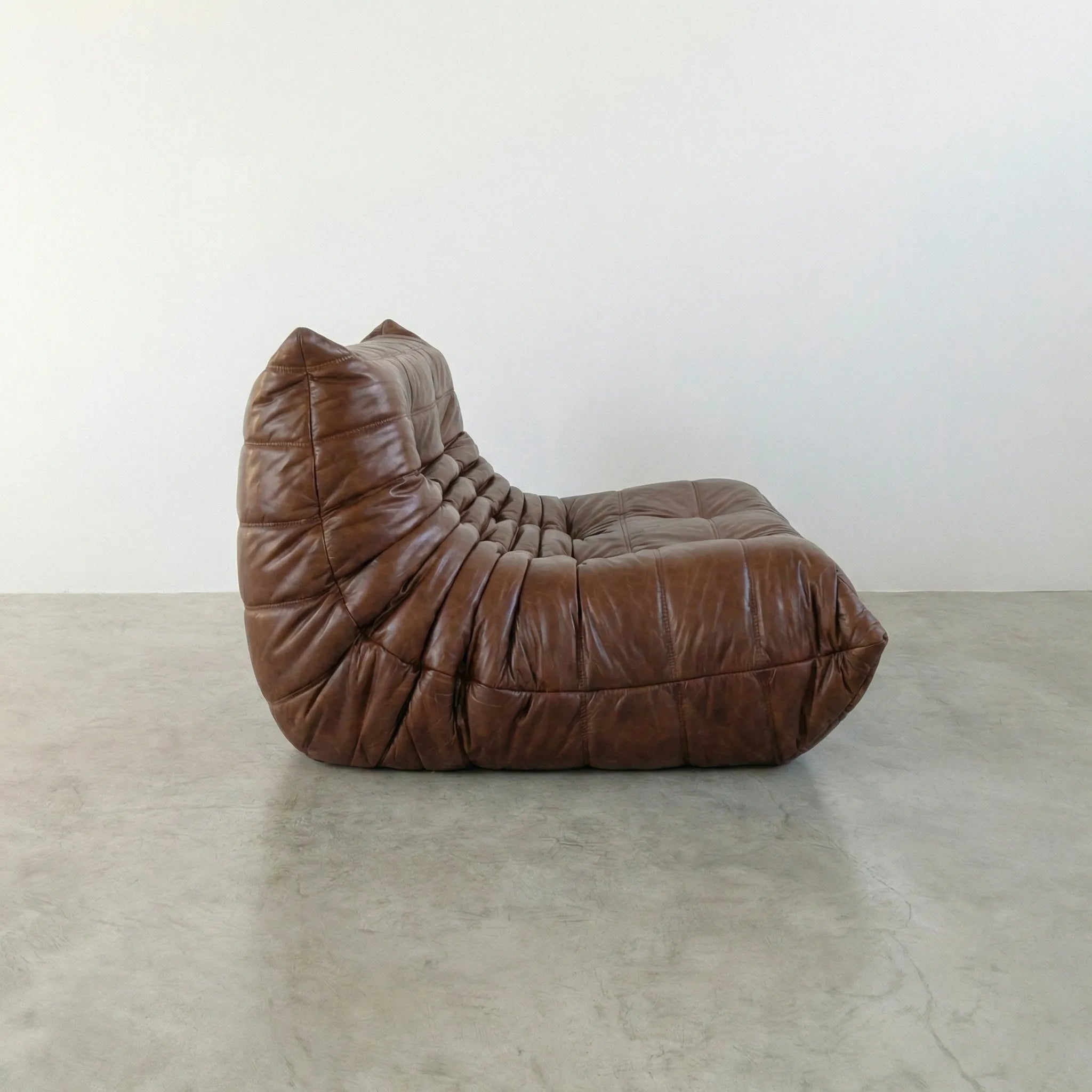 Brown togo sofa in leather on a concrete floor with a white wall background