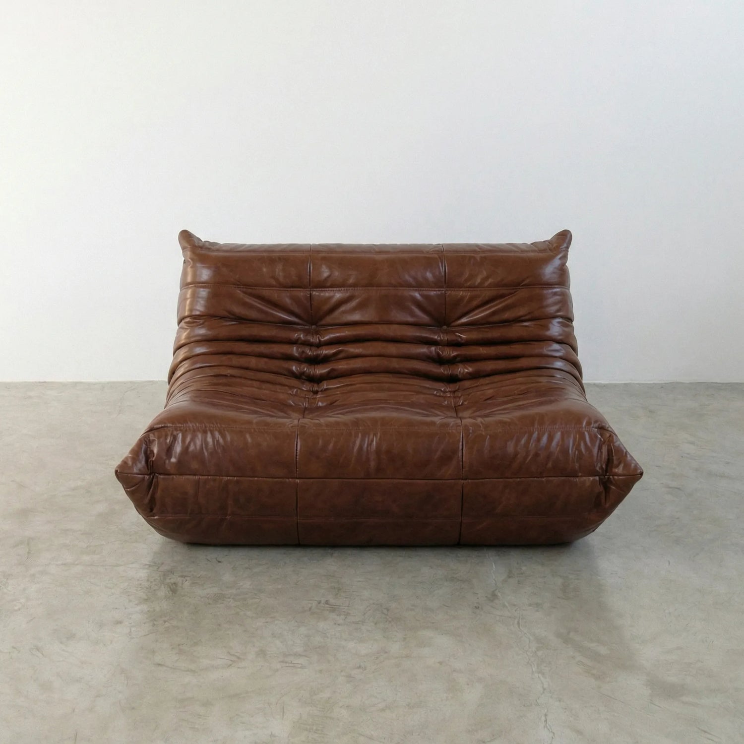 Brown togo sofa in leather on a concrete floor with a white wall background