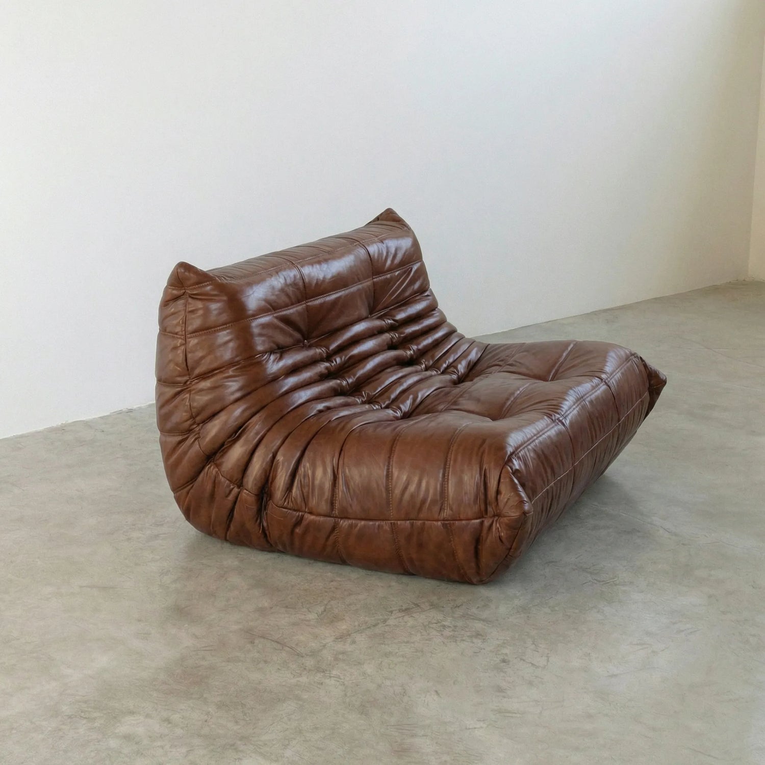 Brown togo sofa in leather on a concrete floor with a white wall background