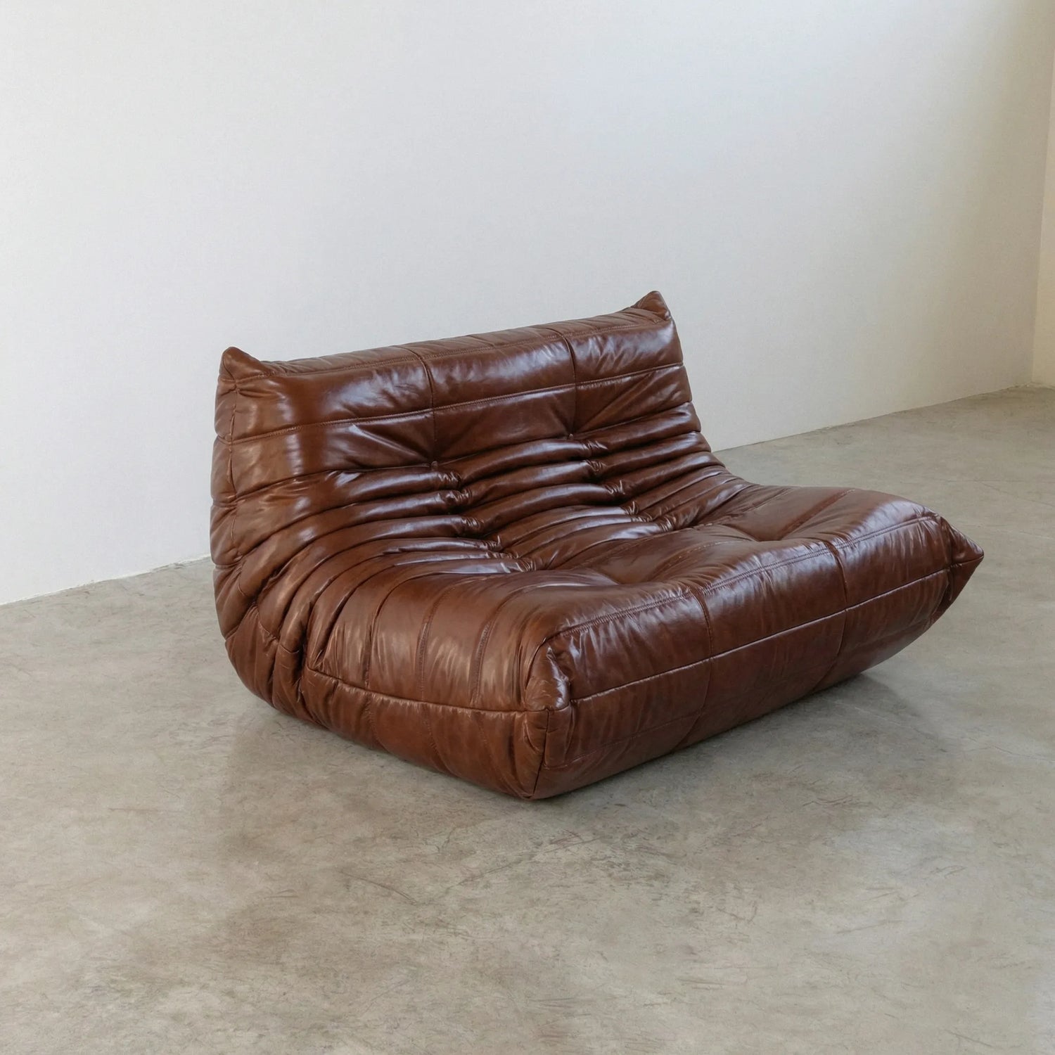 Brown togo sofa in leather on a concrete floor with a white wall background