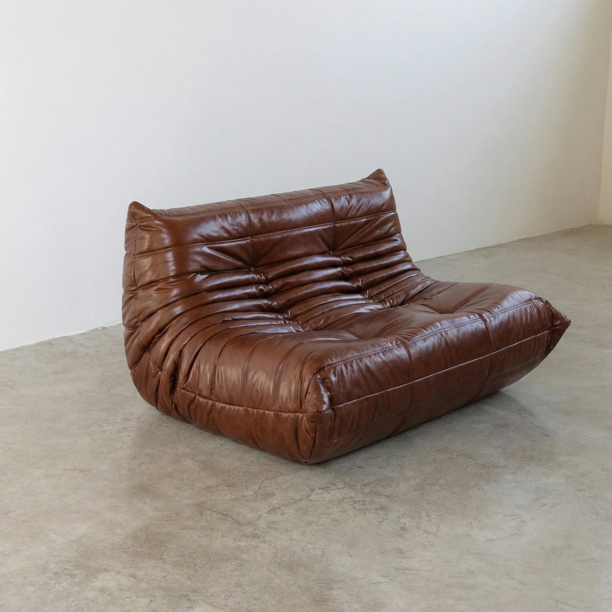 Brown togo sofa in leather on a concrete floor with a white wall background