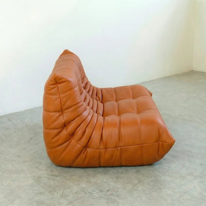 Orange leather togo sofa dupe on a concrete floor with a white wall background
