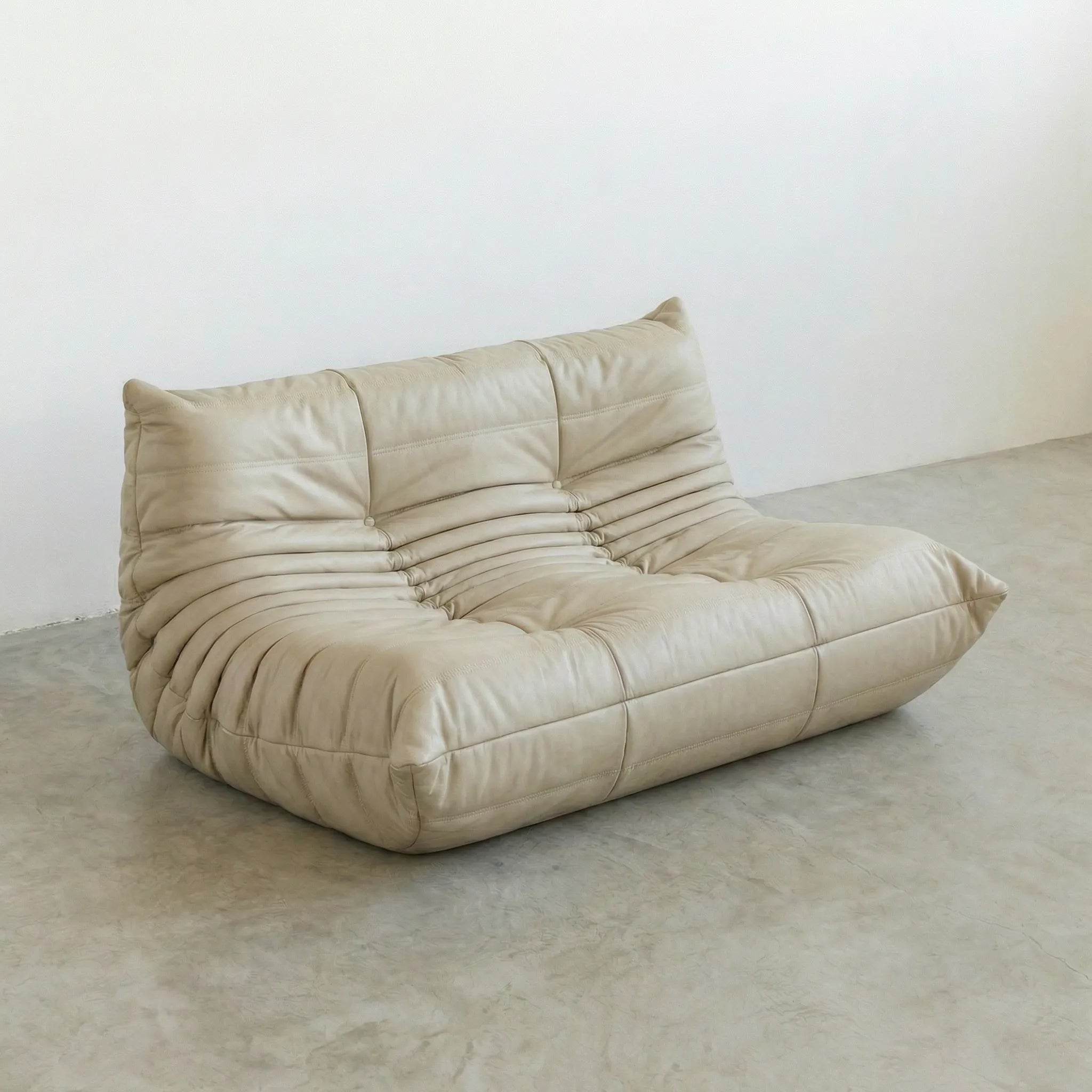 Beige togo sofa dupe on a concrete floor with a white wall background