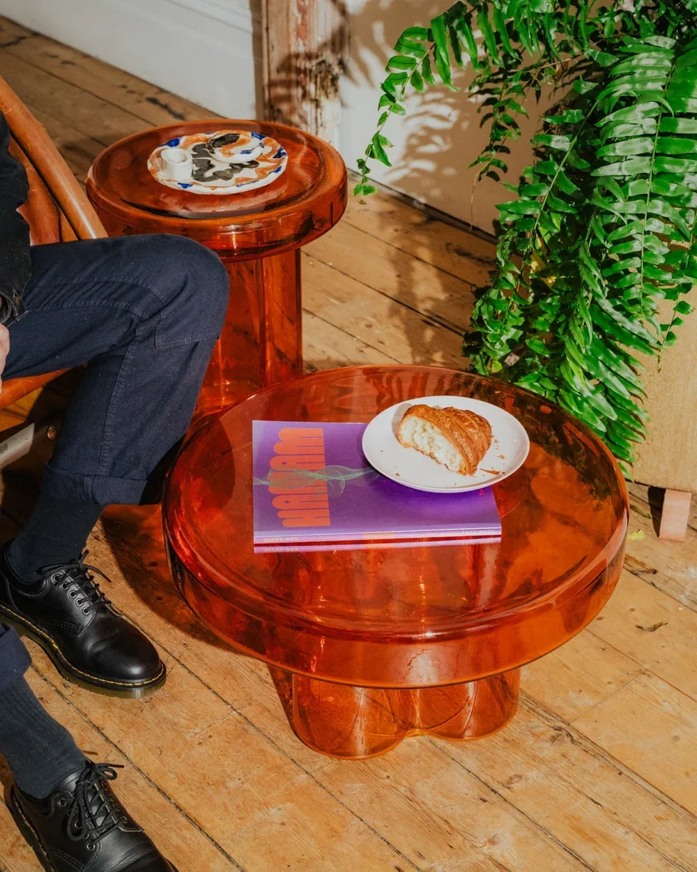 Amber glass side tables with books and a plate beside houseplants.