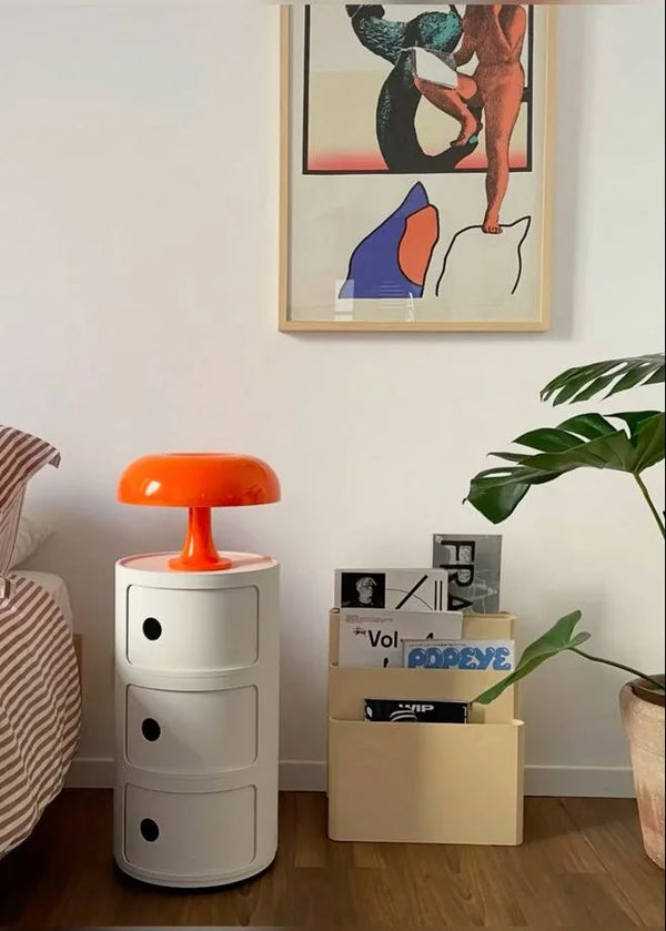 Orange mushroom table lamp on a white cylindrical storage unit.