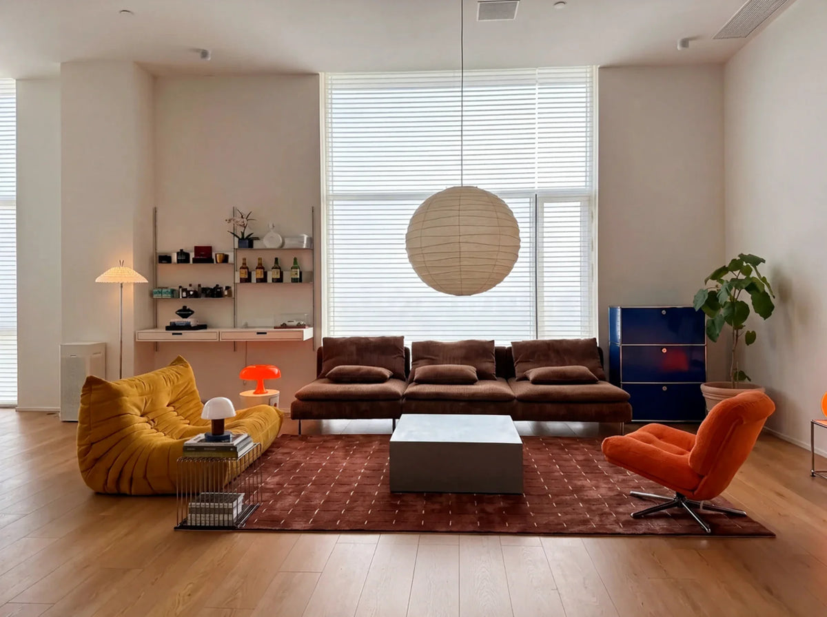 Living room with yellow and orange lounge chairs, a brown sofa and a paper globe pendant.