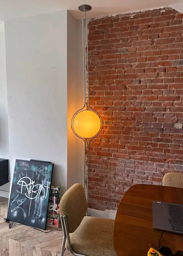 Glowing Zuru floor-to-ceiling lamp beside an exposed brick wall.